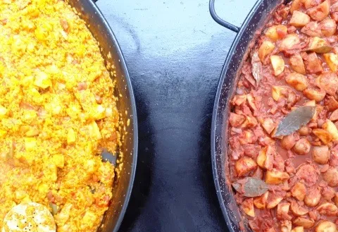 Over head view of two lage paella pans one with paella and the other with patatas bravas