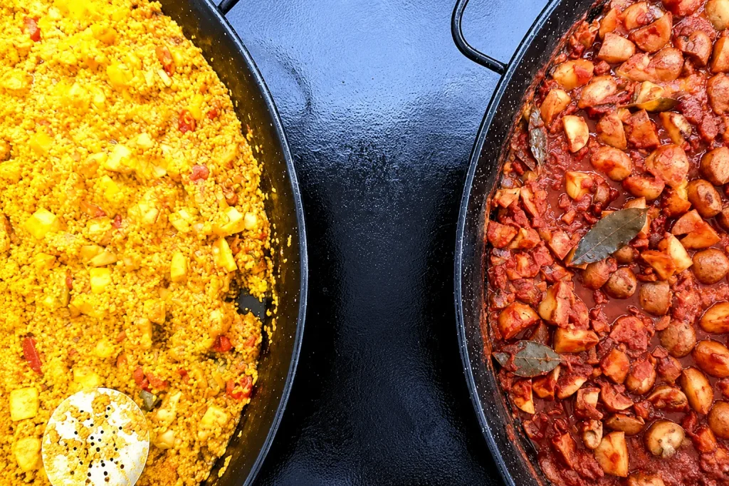 Overhead view of two traditional paella pans, one filled with authentic chicken paella and the other with homemade Patatas Bravas, freshly prepared by Your Paella.